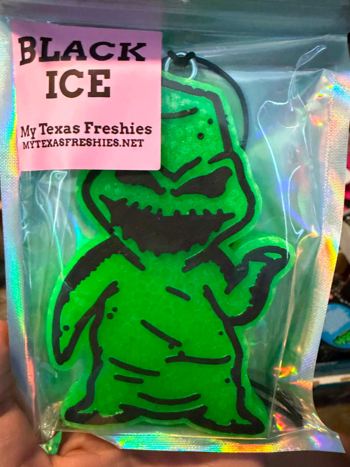 A bright neon green monster-shaped air freshener or car freshie in clear packaging with a pink label reading 'BLACK ICE' and 'My Texas Freshies'.