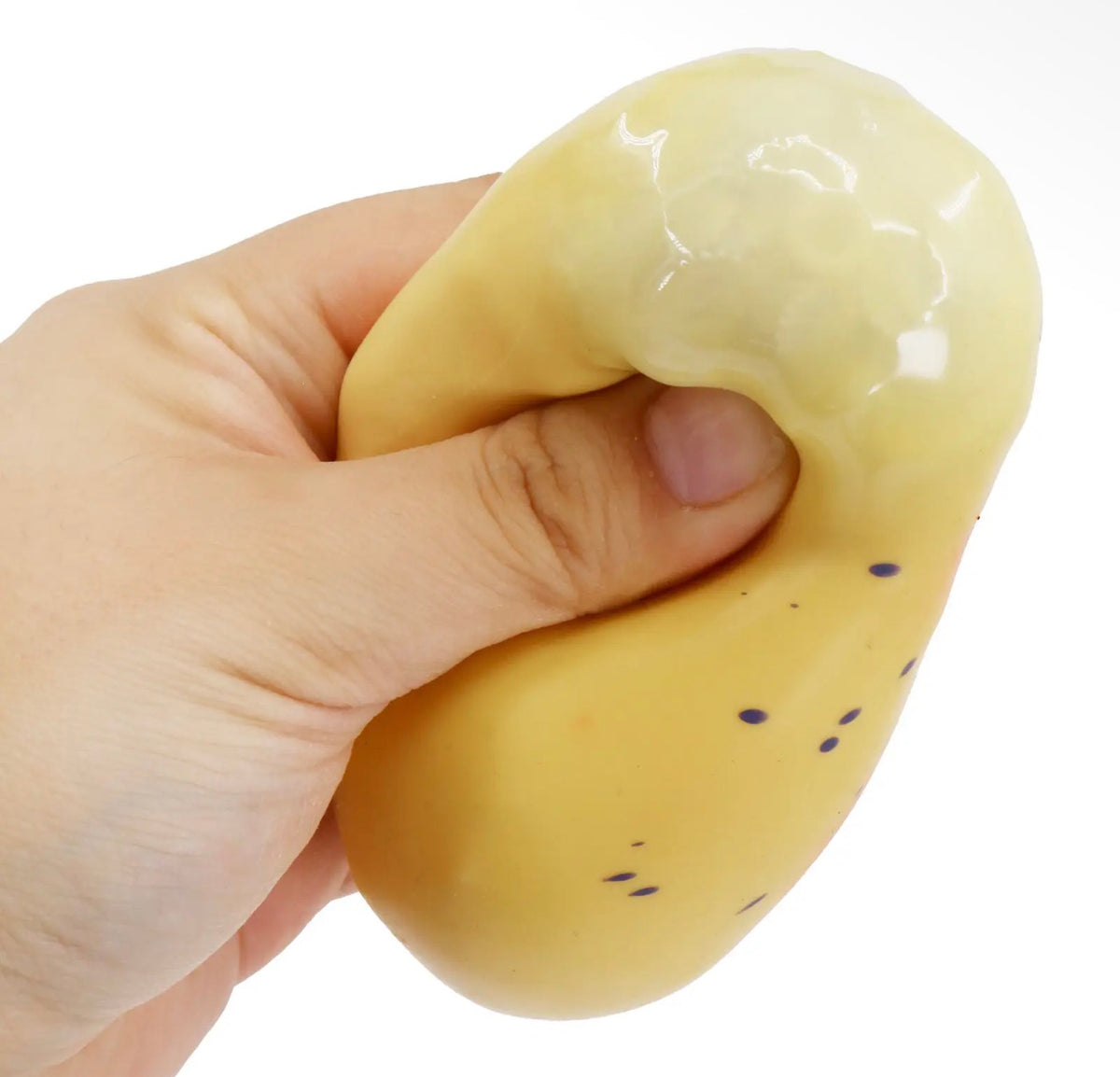 A hand squeezing a glossy, pale yellow squishy toy with small dark blue dots, shown against a plain white background.
