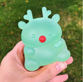 A hand holding a translucent mint green reindeer-shaped object with a red nose against a blurred green grass background.