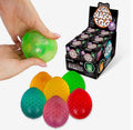 A hand holds a green textured sugar dragon egg toy, with several other colorful dragon eggs and a black display box of Sugar Dragon Eggs on a white background.