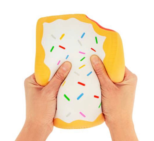 A person's hands squeezing a soft, squishy toy shaped like a slice of toast or a donut with yellow edges, white frosting, and colorful sprinkles, isolated on a white background.