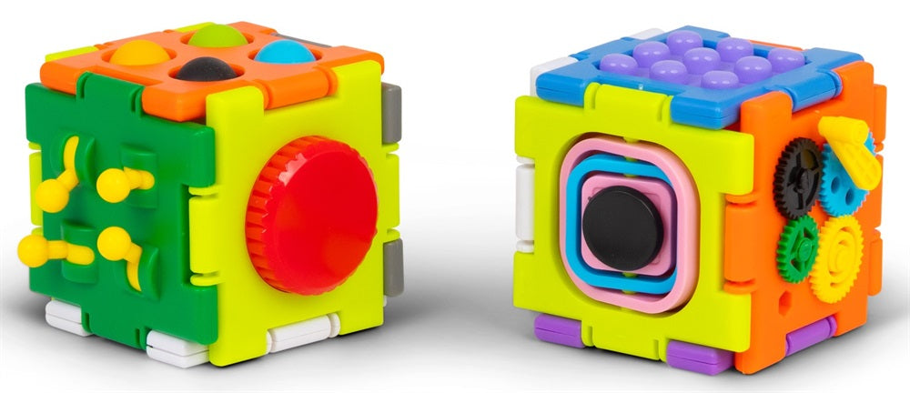 Two colorful plastic sensory cubes shown on a light gray studio background. The left cube displays multiple textured faces including a red circular dial, yellow pegs, and a green panel.