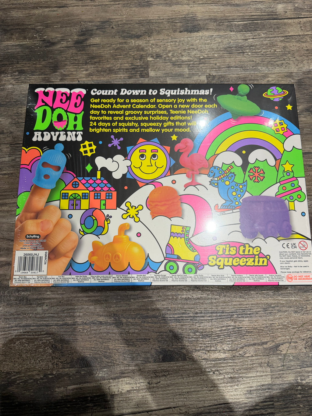 Nee Doh Advent 'Tie the Squeezin'' toy box shown from the back, featuring a colorful illustrated design with a hand pressing a blue squishy, set on a dark wood floor.