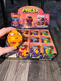 A hand holds a yellow Press Gyroball toy in front of a retail display box filled with packaged mini blind balls. The display box is branded Avengers Press Gyroball and shows multiple colorful ball designs.