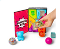 A colorful toy surprise box with a hand reaching in to grab a small translucent bear-shaped toy. The open box shows bright compartments labeled with question marks, and several loose toys are scattered around on a white background.