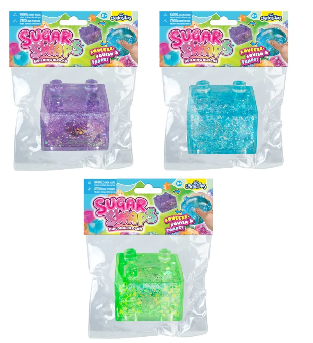 Three packaged squishy blocks from Craziest Toys, each in a clear plastic bag with a colorful header card. The packages show purple glitter, bright blue glitter, and neon green glitter squishy toys.