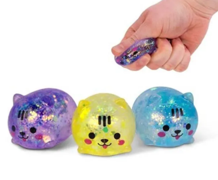 Three colorful glitter-filled cat squishy toys in purple, yellow, and blue, with a hand squeezing the purple squishy above them.