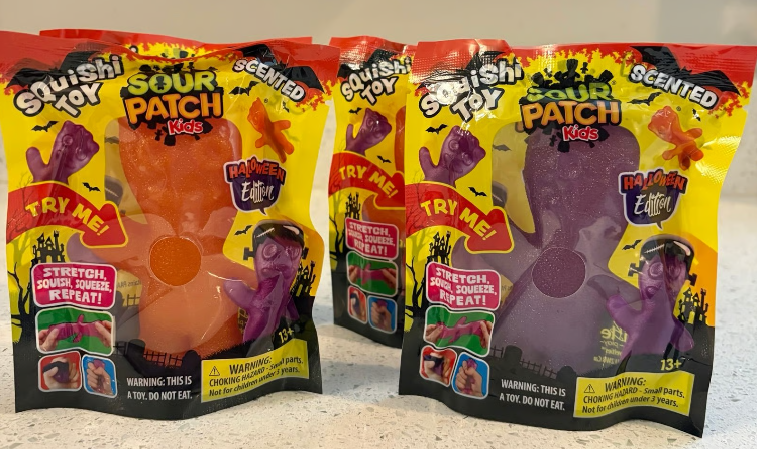 Two packages of Squishy Toy Sour Patch Kids Halloween Edition, one orange and one purple, displayed on a light-colored surface.
