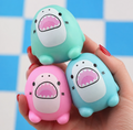 Three cute shark-shaped squishy stress toys in mint green, light blue, and pink, held in a hand against a blue and white checkered background.