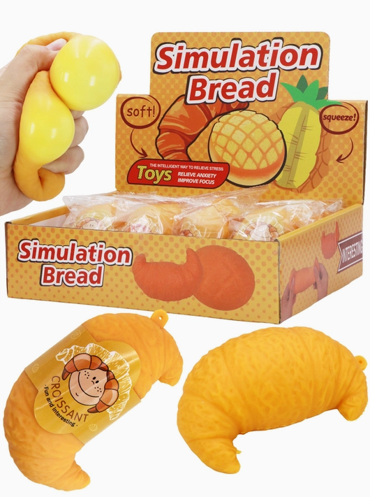 Simulation bread toy set including a croissant and a pineapple-shaped toy, with a hand squeezing a yellow bread-like toy. A display box and individual packages labeled 'Simulation Bread' are shown on a white background.