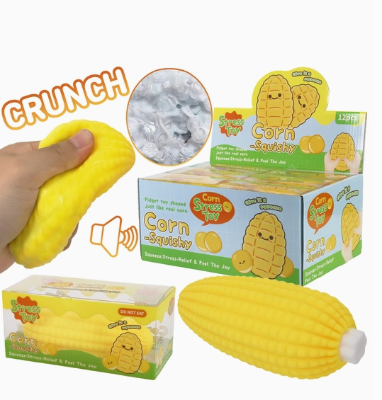 A yellow corn-shaped squishy toy shown with its retail packaging and a hand squeezing it. The packaging features cartoon corn graphics and the text 'Corn Squishy' and 'Summer Stress Relief & Fun The Joy'.
