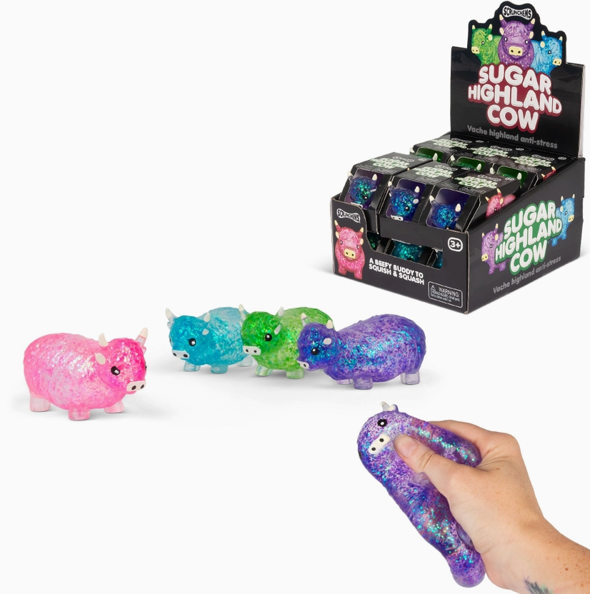 A display box of Sugared Highland Cows, with several small glittery cow figures in pink, blue, green, and purple shown on a white background, plus a hand holding a purple glittery cow.
