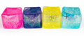 Four translucent glittery ice cube-shaped ornaments in pink, blue, yellow, and aqua, arranged in a row on a white background.