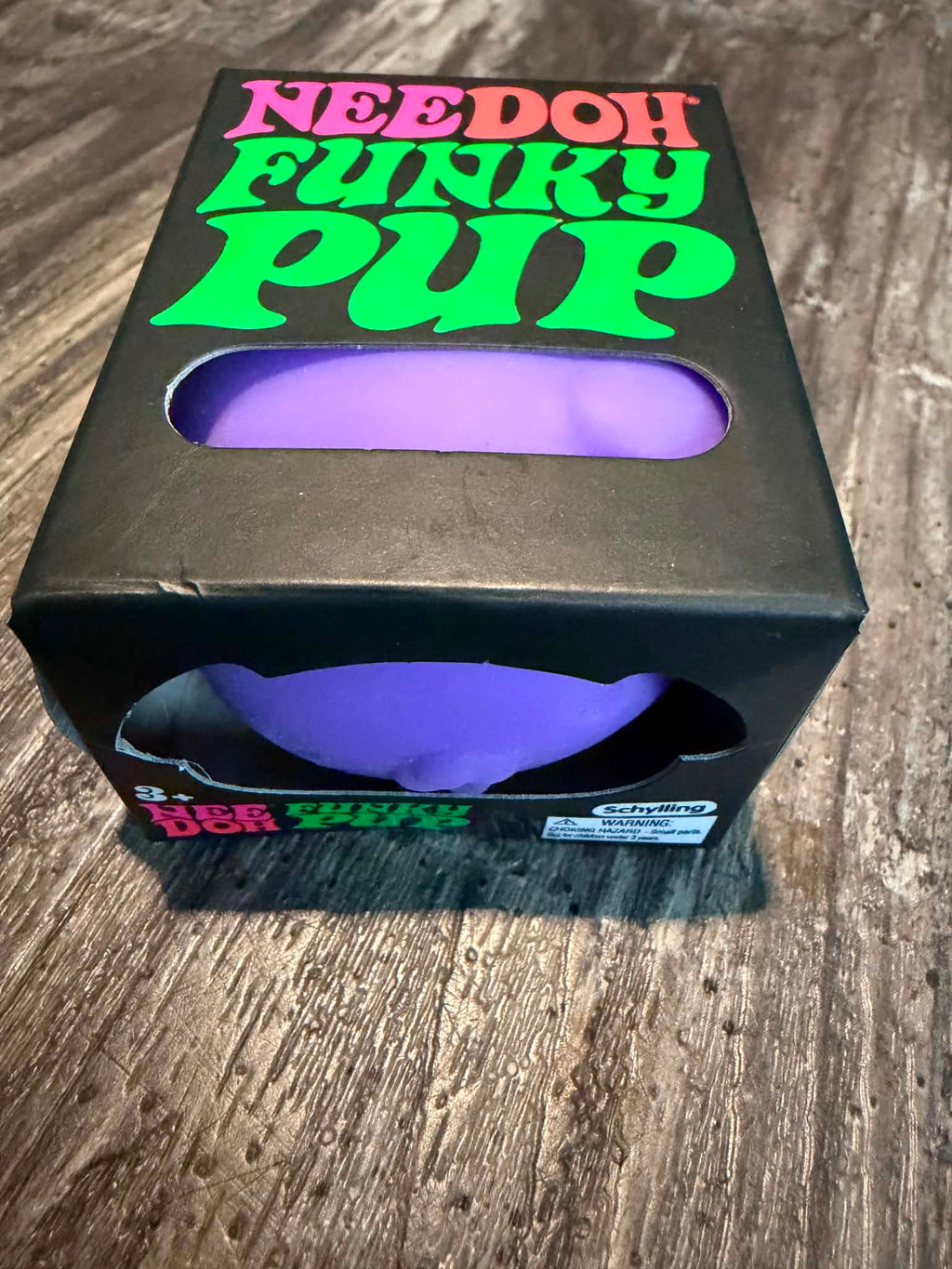 A black novelty box labeled 'NEEDOH FUNKY PUP' with a purple curved insert visible through cutouts, photographed on a wood surface.