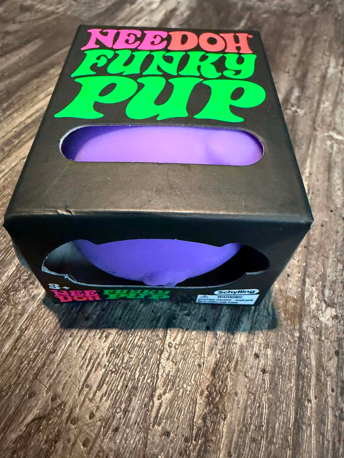 A black novelty box labeled 'NEEDOH FUNKY PUP' with a purple curved insert visible through cutouts, photographed on a wood surface.