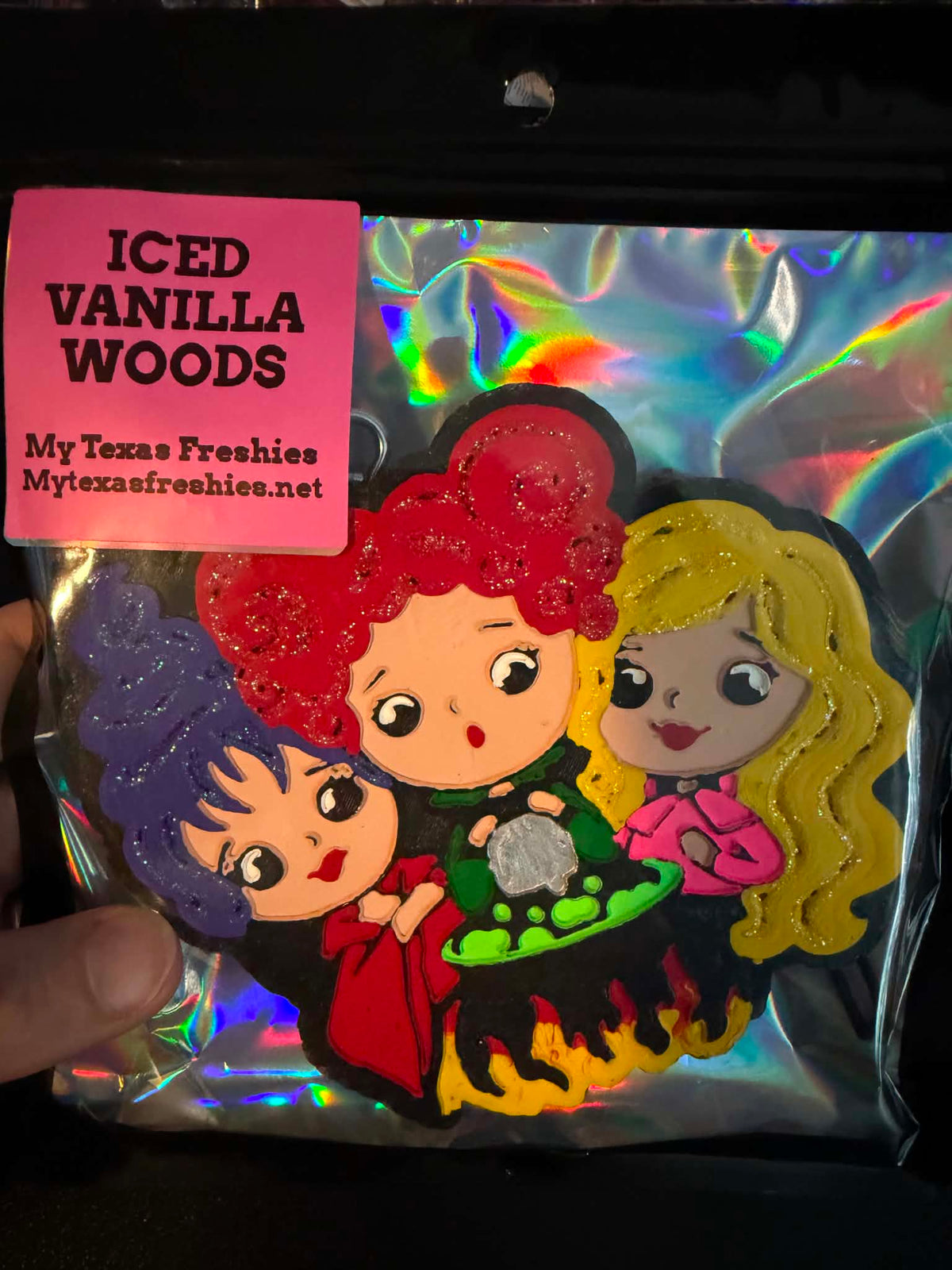 A packaged novelty patch or applique featuring three cartoon witch characters with purple, red, and yellow hair standing by a cauldron, sealed in a clear plastic bag with a pink sticker reading 'ICED VANILLA WOODS' and 'My Texas Freshies MyTexasFreshies.net'.