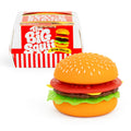 A small toy hamburger figurine with a sesame seed bun, red tomato slice, brown patty, yellow cheese, and green lettuce, shown in front of its red-and-white branded box labeled 'The Big Squishy'.
