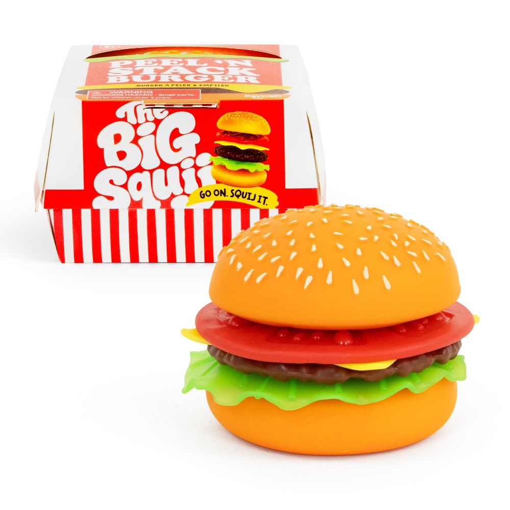 A small toy hamburger figurine with a sesame seed bun, red tomato slice, brown patty, yellow cheese, and green lettuce, shown in front of its red-and-white branded box labeled 'The Big Squishy'.